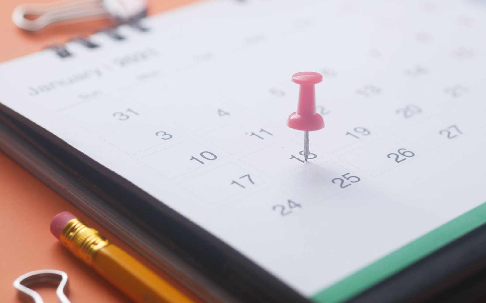 A pink pushpin marks a date on a January calendar page beside a pencil